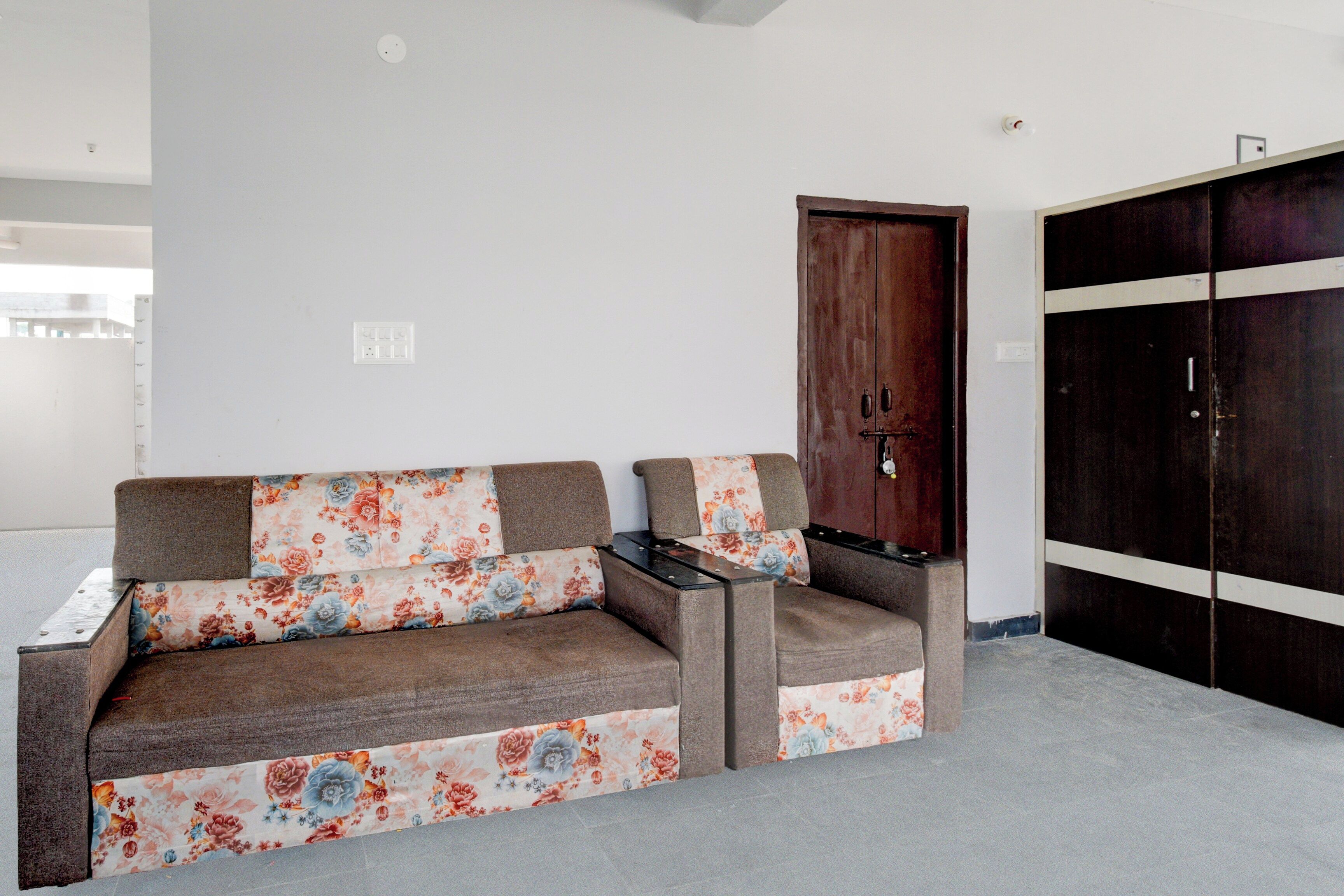 A sofa with floral upholstery, a wooden door, and a wardrobe with horizontal stripes.