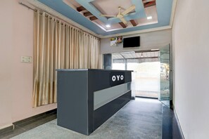 A reception desk with a sign that reads 'OYO' in a hotel lobby with a ceiling fan, a window with curtains, and a wall-mounted television. - Hotel O by OYO Sansar (Hyderabad)