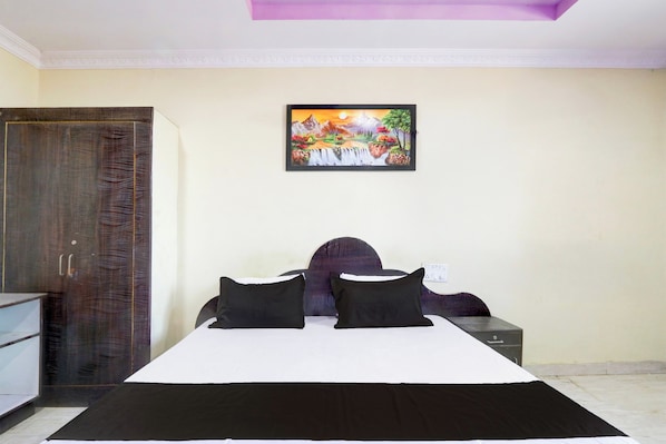 A bedroom with a bed, two pillows, a nightstand, a painting, and a wardrobe. - Hotel O by OYO Sansar (Hyderabad)