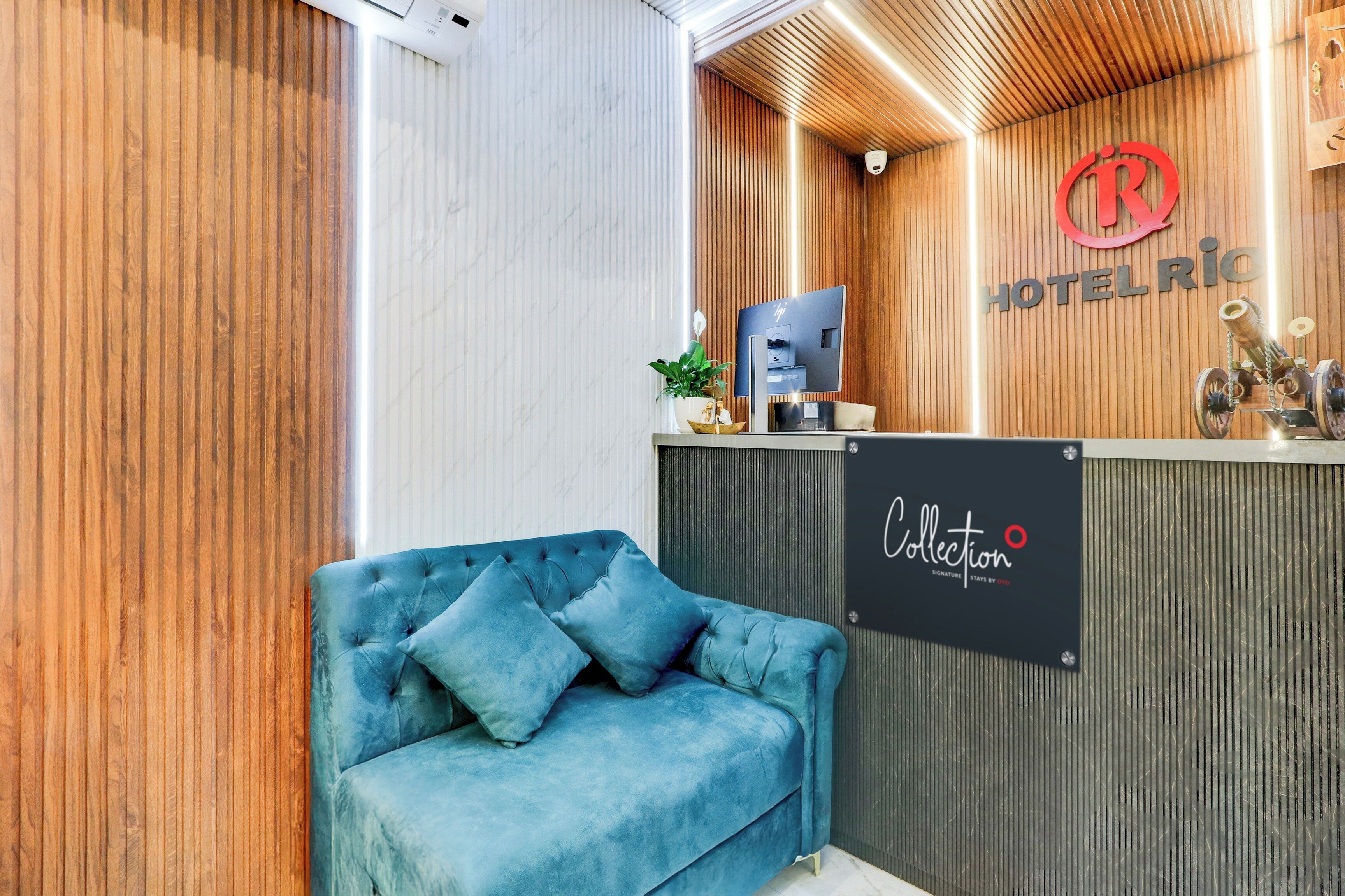 Zona de recepción de un hotel con un mostrador de madera, un sofá azul y un cartel que dice 'HOTEL RIO Collection'.