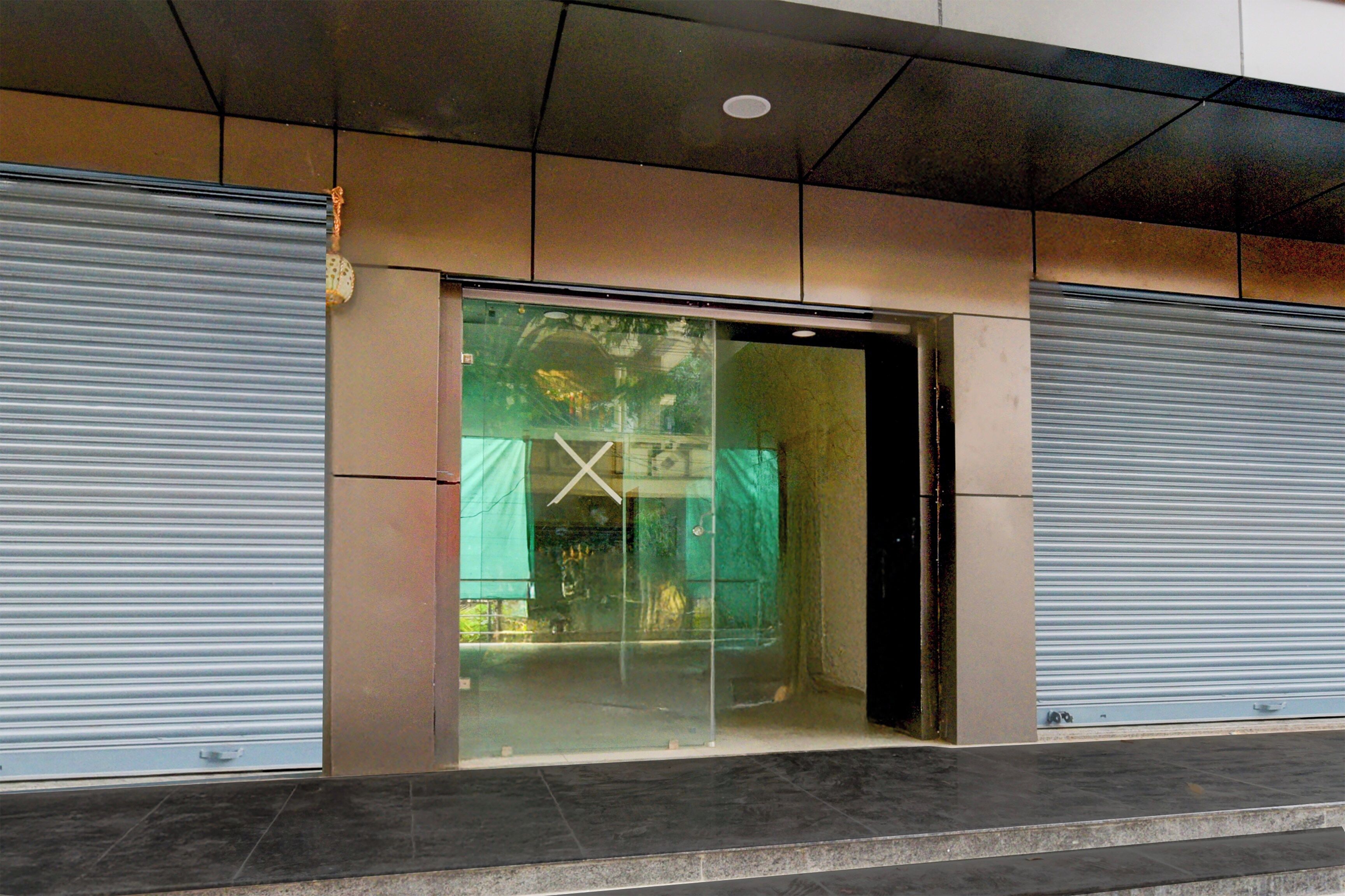 A building entrance with closed metal shutters, a glass door, and a tiled floor.
