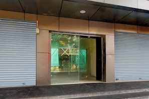 Entrada de un edificio con persianas metálicas cerradas, un escaparate de vidrio y piso de baldosas.