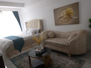 Une chambre à coucher moderne avec un lit, un canapé, une table basse et un tableau accroché au mur.