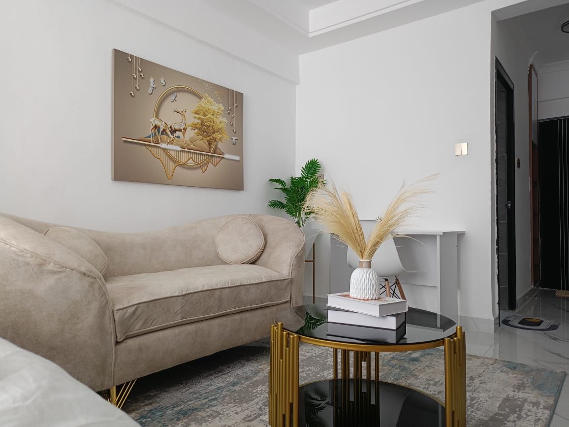 Un salon moderne avec un canapé beige, une table basse en verre aux pieds dorés et un tableau décoratif accroché au mur.