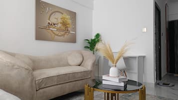 Un salon moderne avec un canapé beige, une table basse en verre aux pieds dorés et un tableau décoratif accroché au mur.