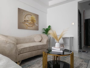 Un salon moderne avec un canapé beige, une table basse en verre aux pieds dorés et un tableau décoratif accroché au mur.
