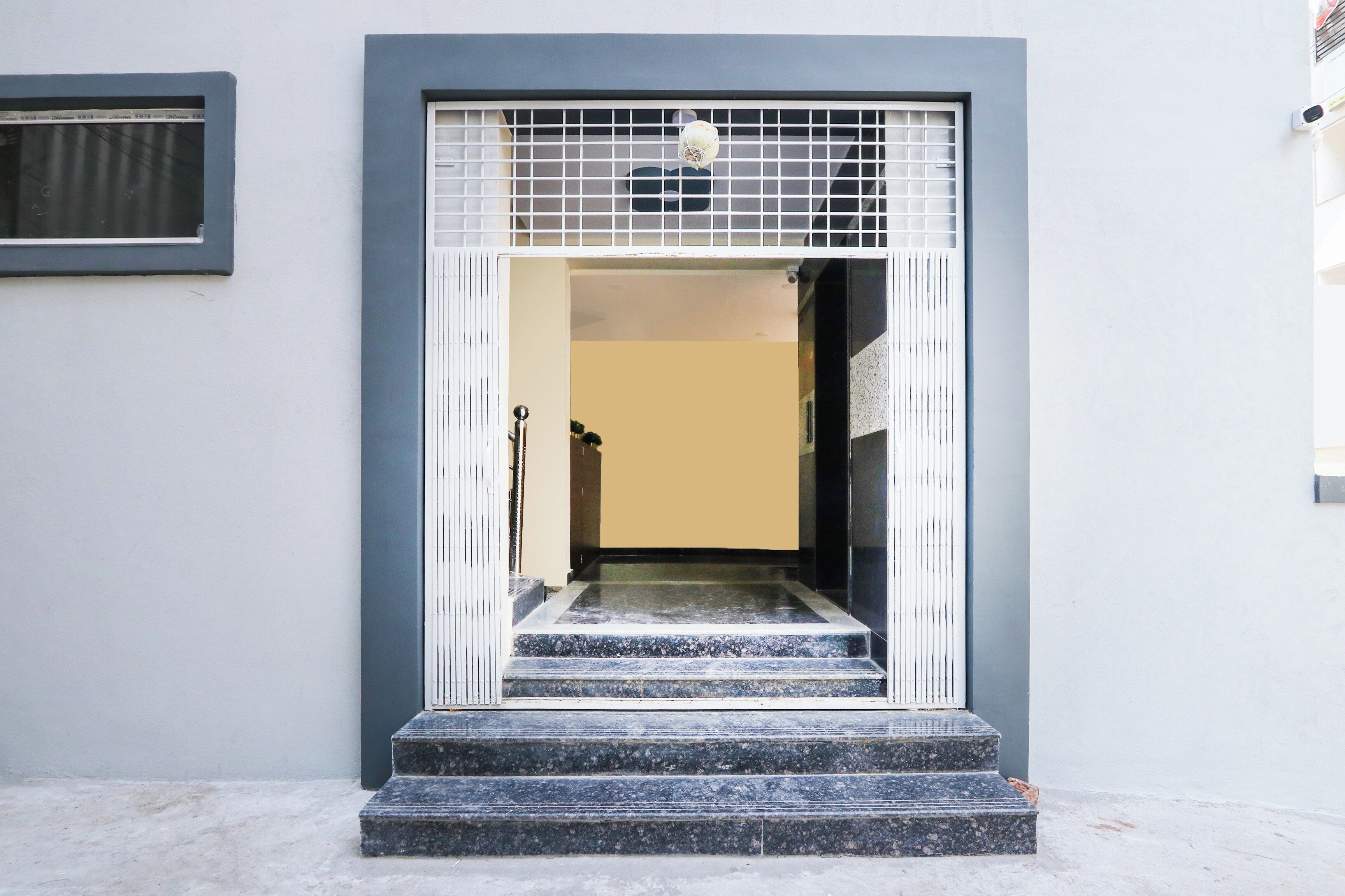 Una entrada de edificio con una reja metálica, unas escaleras que conducen a una puerta y un ventanal encima de la puerta.