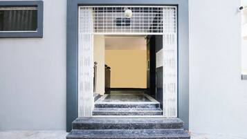 Ein Gebäudeeingang mit einem Metallgitter, einer Treppe, die zu einer Tür führt, und einem kleinen Fenster darüber.