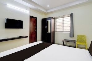A hotel room with a bed, a television mounted on the wall, a window with curtains, and a small table with a chair. - Hotel O by OYO ELEGANT NEST Lemon Tree (Hyderabad)