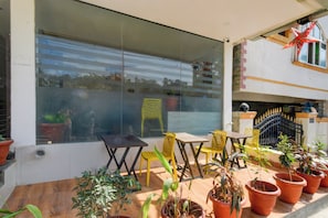 An outdoor seating area with tables and chairs, potted plants, and a view of the street through a large window. - Hotel O by OYO ELEGANT NEST Lemon Tree (Hyderabad)