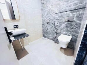 A bathroom with a white sink, a toilet, and a shower area with marble walls. - Hotel Rajsi Inn (Faizabad)