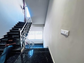 A staircase with a handrail, a window at the top, and a light switch on the wall. - Hotel Rajsi Inn (Faizabad)