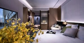 Quarto de hotel moderno com uma cama grande, área de estar e vista para um edifício.