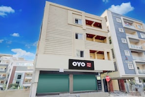 A multi-story hotel with a flat facade, balconies, and a green shuttered entrance. - Hotel O Vega (Hyderabad)