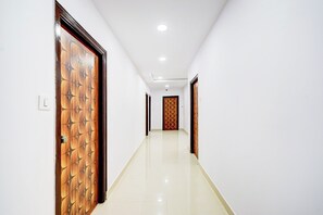 A corridor with wooden doors on both sides, a tiled floor, and a plain white wall. - Hotel O Vega (Hyderabad)
