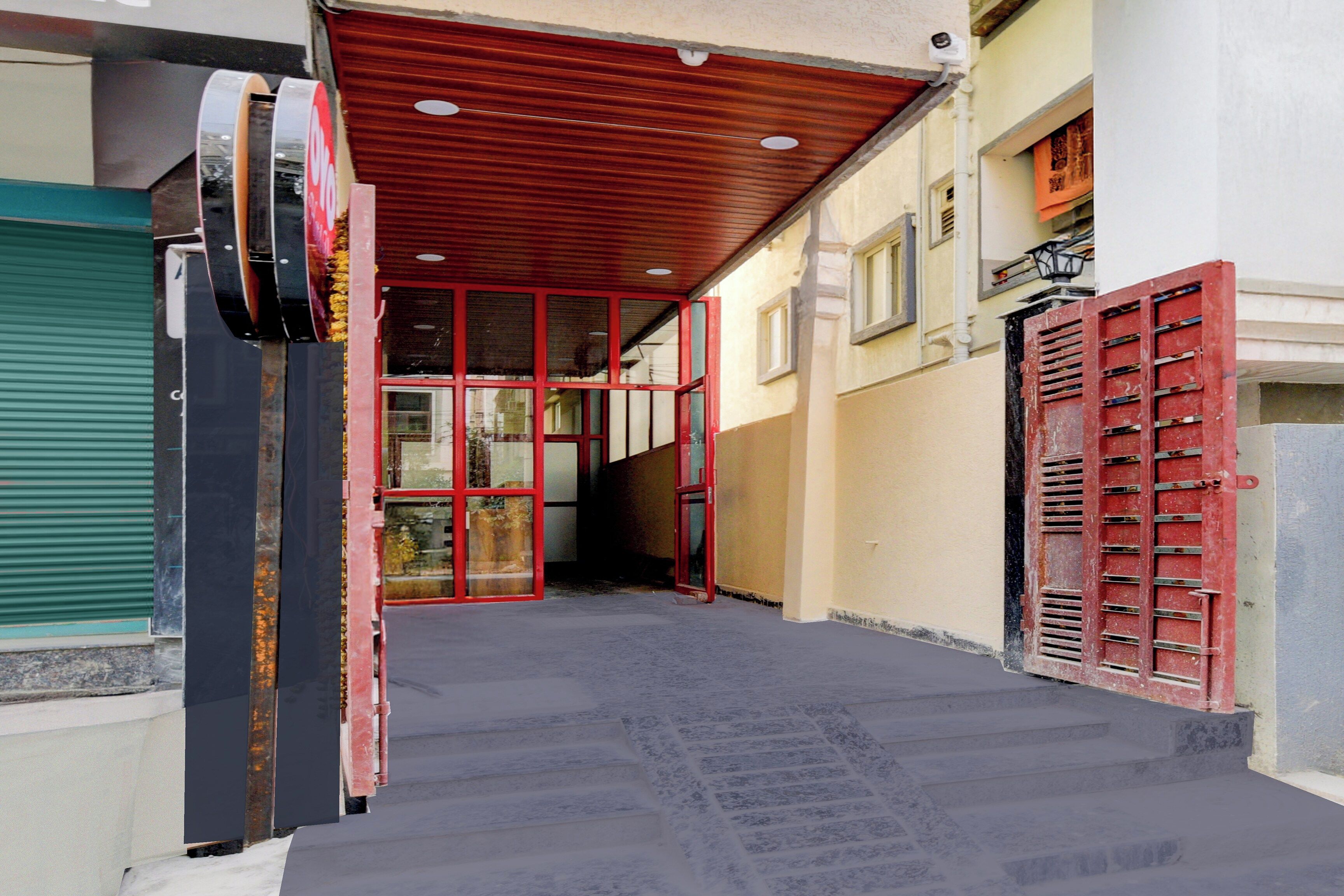 Un couloir étroit, avec un portail en métal rouge et une porte à volets verts.