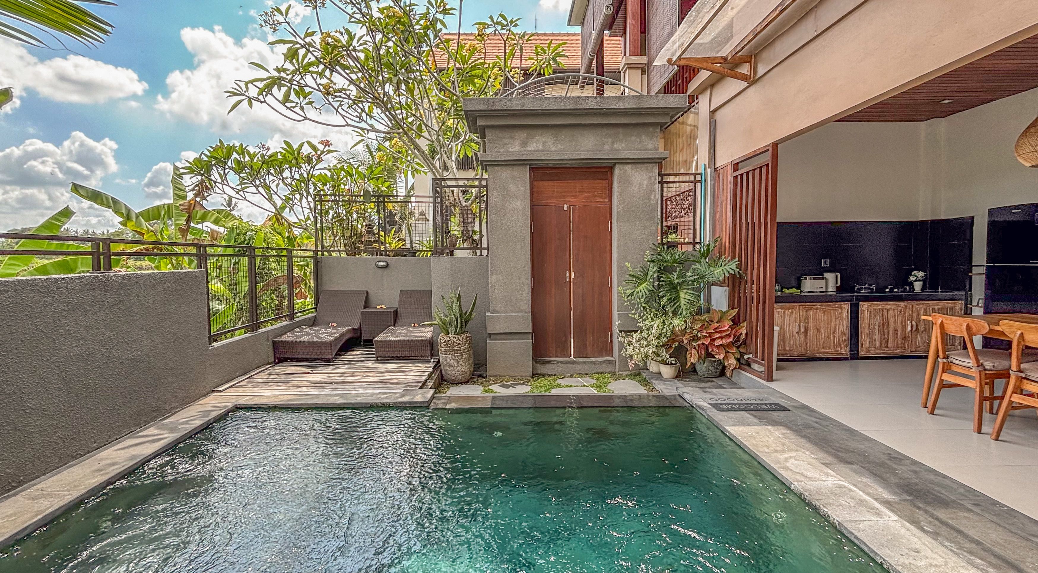 A swimming pool with a stone border, a wooden door, and outdoor seating with cushions.