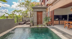 A swimming pool with a stone border, a wooden door, and outdoor seating with cushions. - Villa Laku Singakerta with Kitchenette (Gianyar)