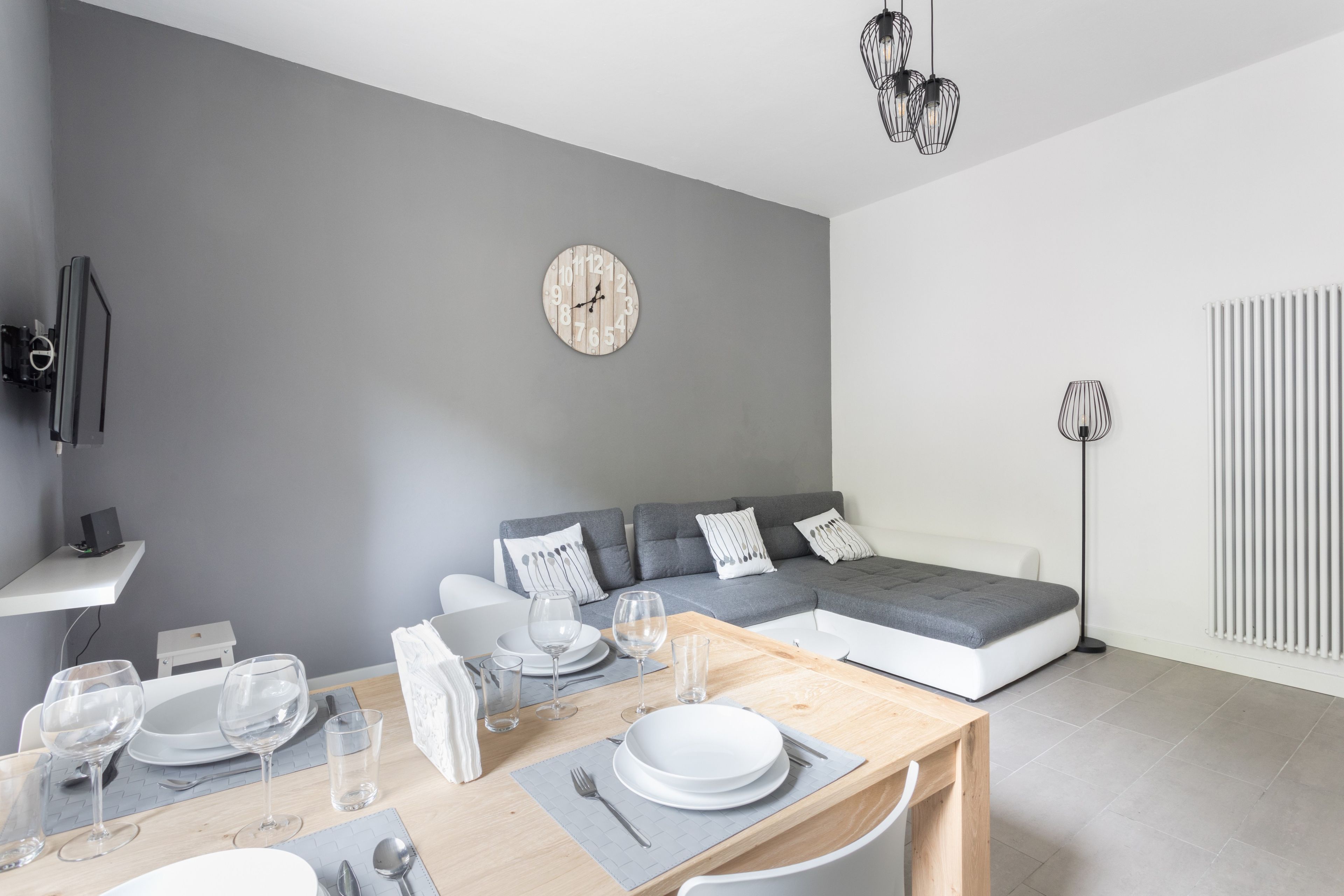 Ein zeitgemäßer Wohnraum mit Essbereich, grauem Sofa und Wanduhr.