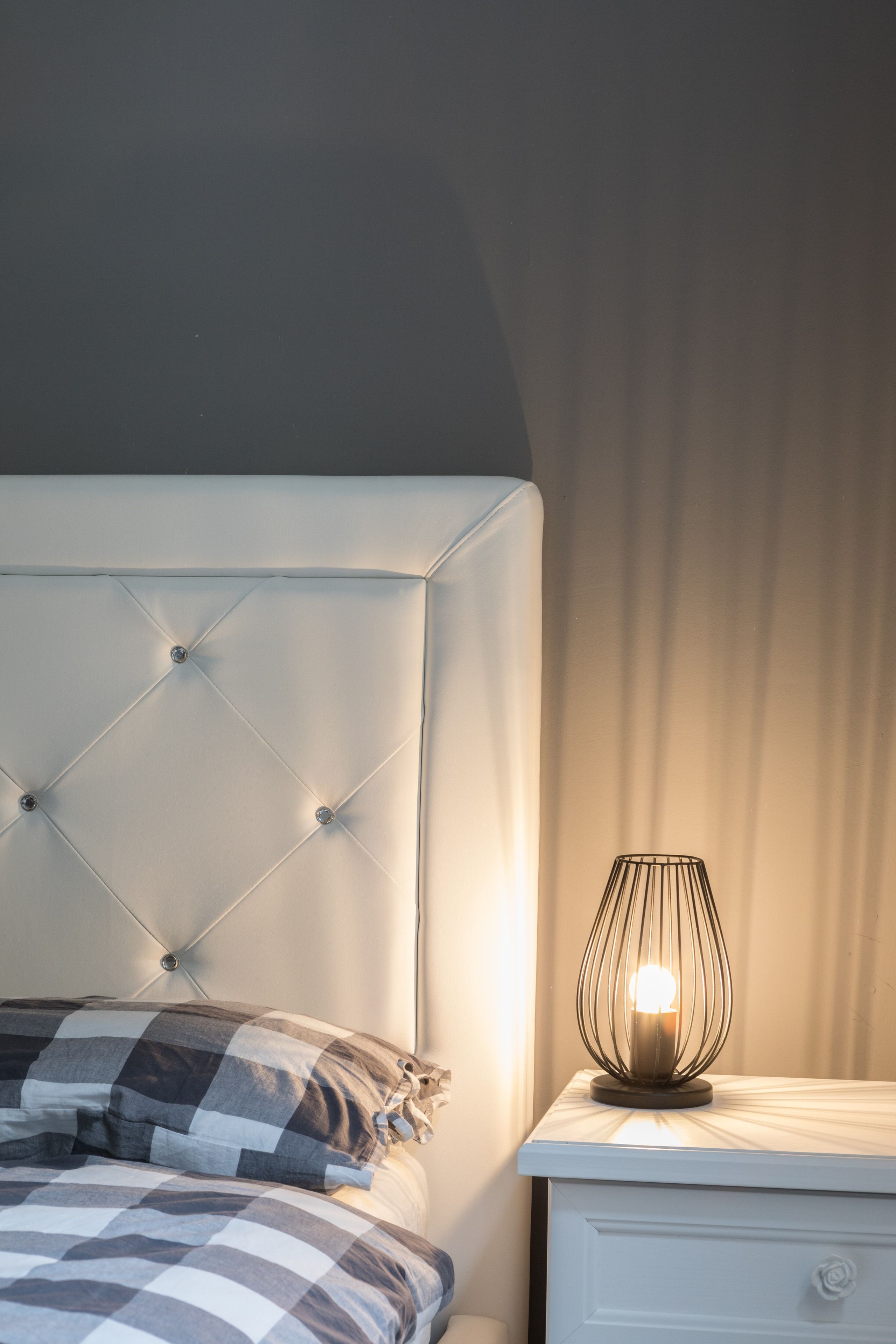 Ein ordentlich bezogenes Bett mit einer karierten Decke und einer Nachttischlampe auf einem weißen Nachttisch.