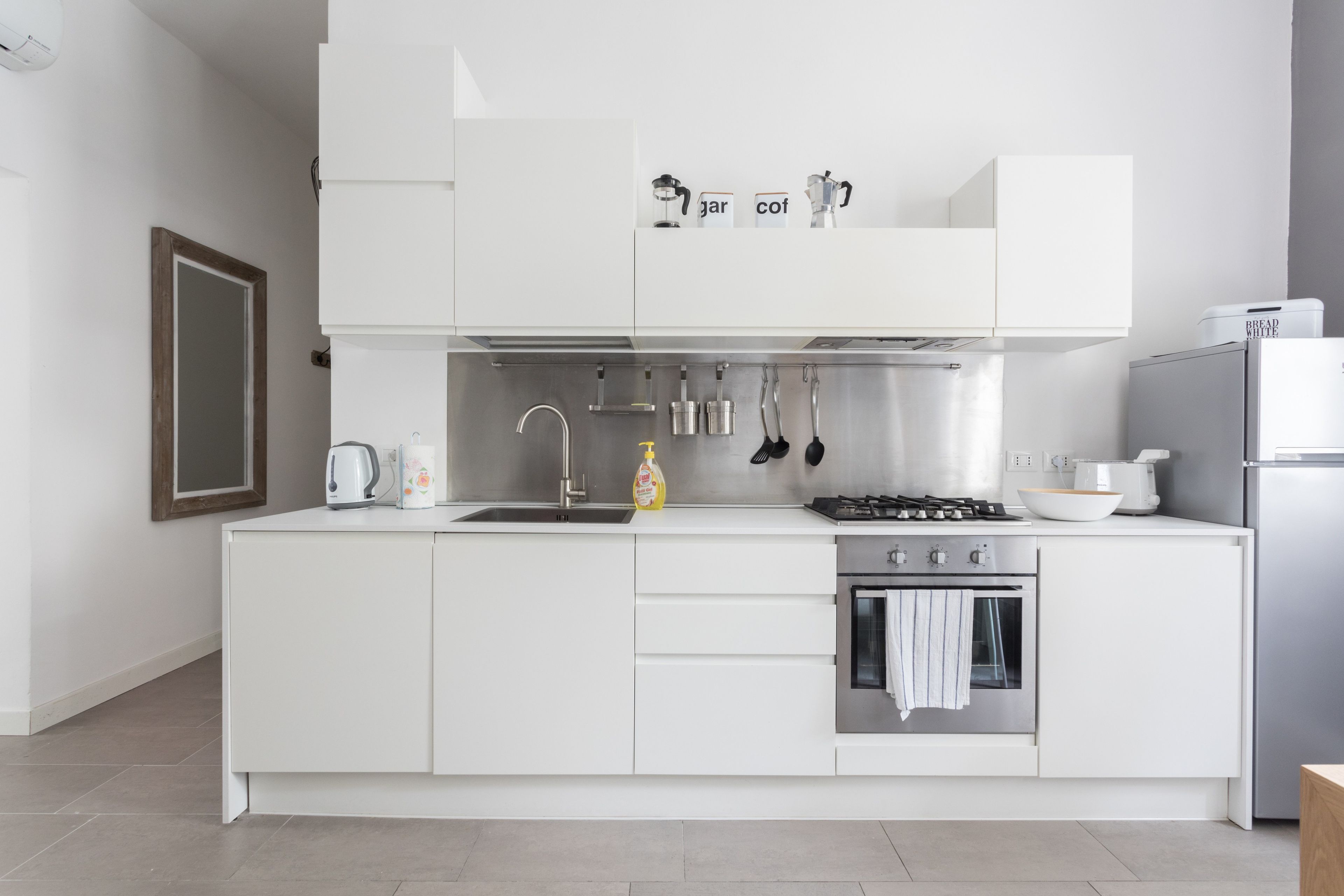 A modern kitchen with white cabinetry, a stainless steel sink, a gas stove, and an oven.
