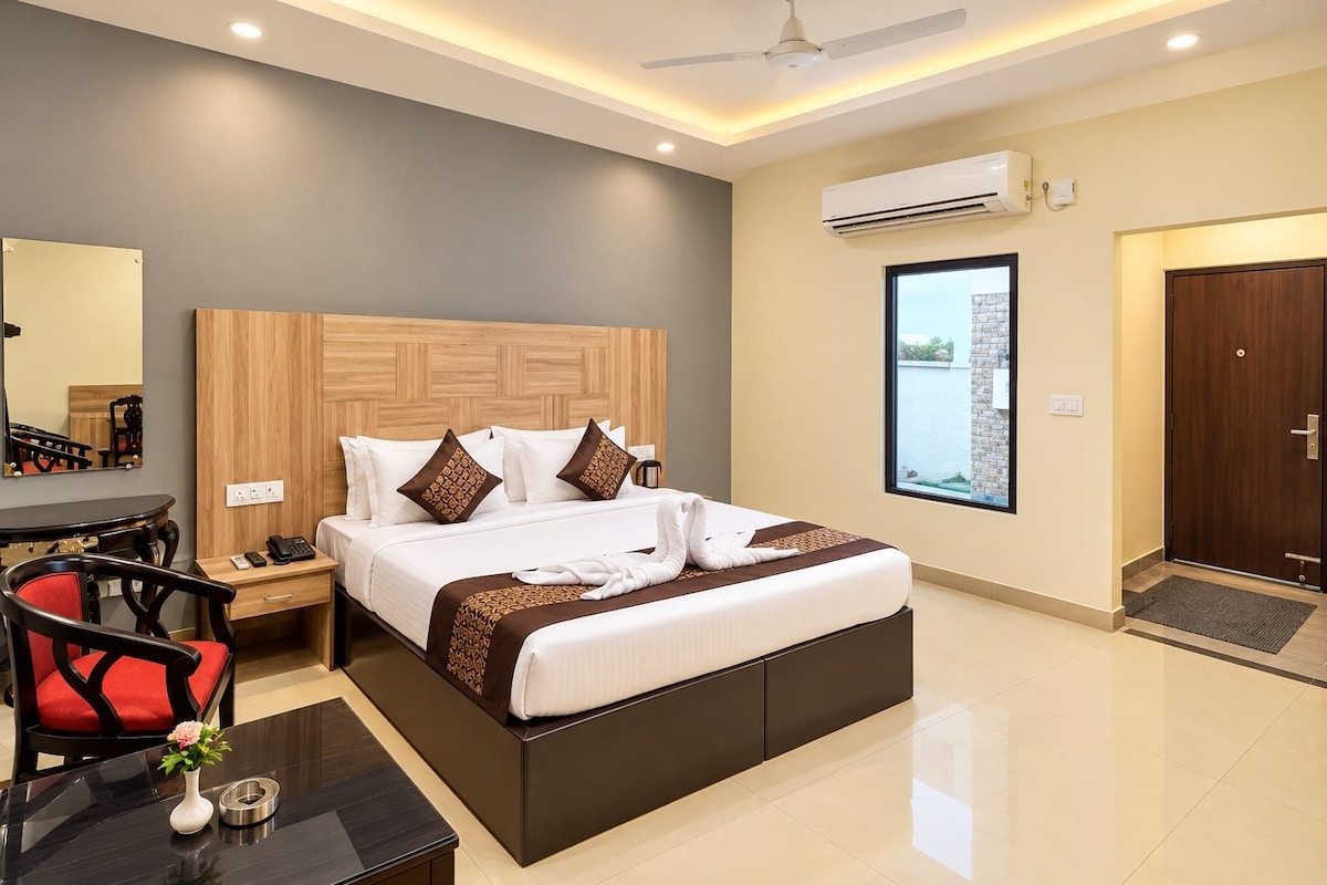 A modern hotel room with a large bed, a desk with a chair, a mirror, and an air conditioning unit.