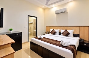 A hotel room with a bed, bedside table, and a desk with a chair. - Eva Hotel (Zirakpur)