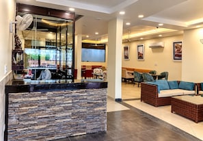 A modern interior with a stone-textured counter, seating area with sofas, and a dining space with chairs and tables. - Eva Hotel (Zirakpur)