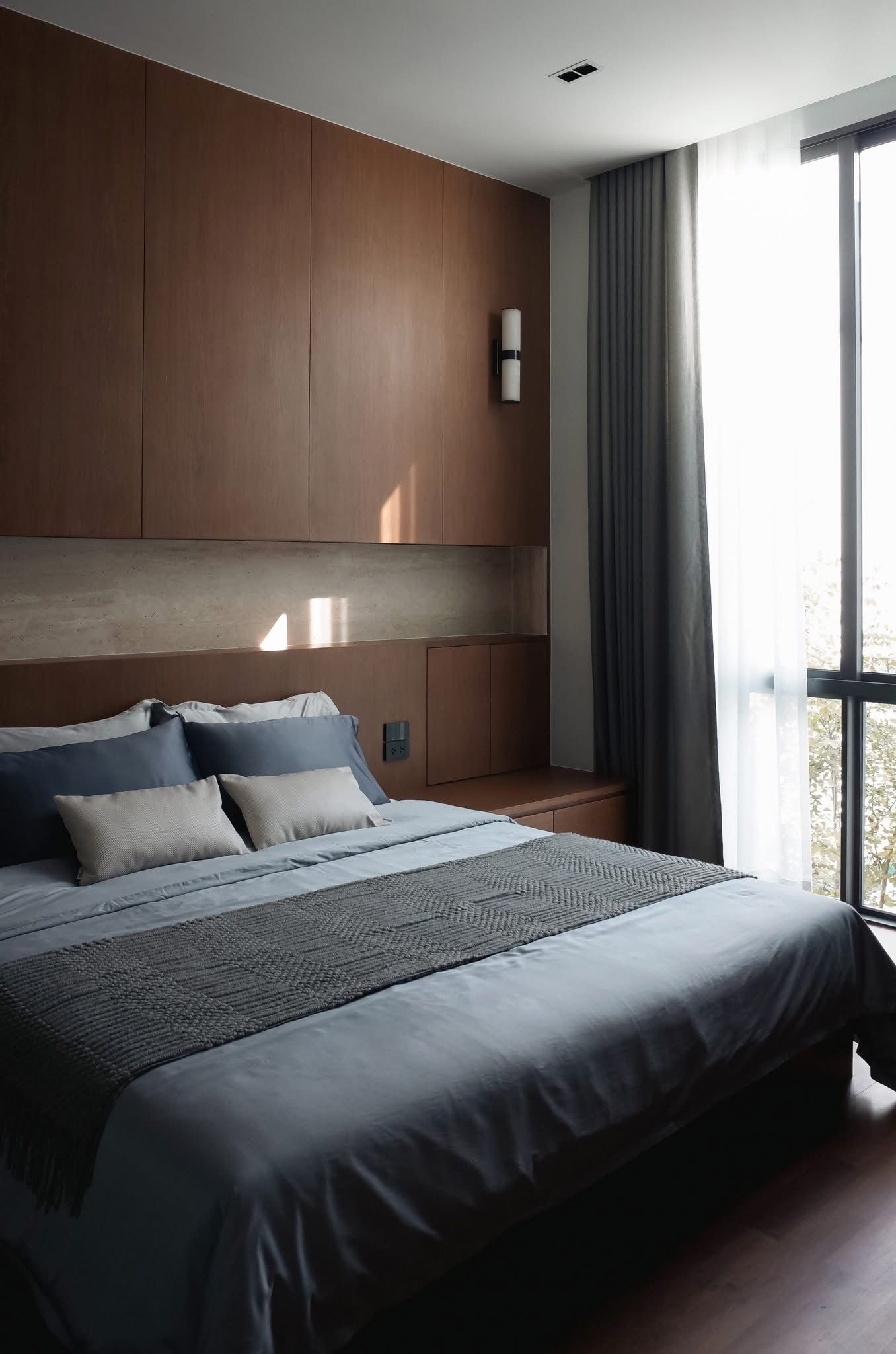 A modern bedroom with a large bed, wooden headboard, and a view of the outdoors through a window.