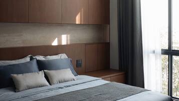 A modern bedroom with a large bed, wooden headboard, and a view of the outdoors through a window.