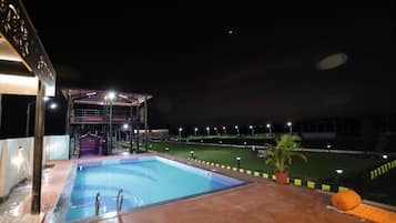 A swimming pool with a covered area, a fenced sports field, and a building with a balcony.