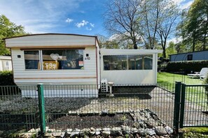 A mobile home with a window displaying a heart design, a small porch, and a fenced yard.