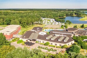 A large building with multiple roofs, surrounded by greenery and a lake.