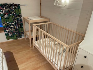 Un berceau pour bébé avec un cadre en bois et un matelas, une petite table de chevet et un luminaire fixé au mur.