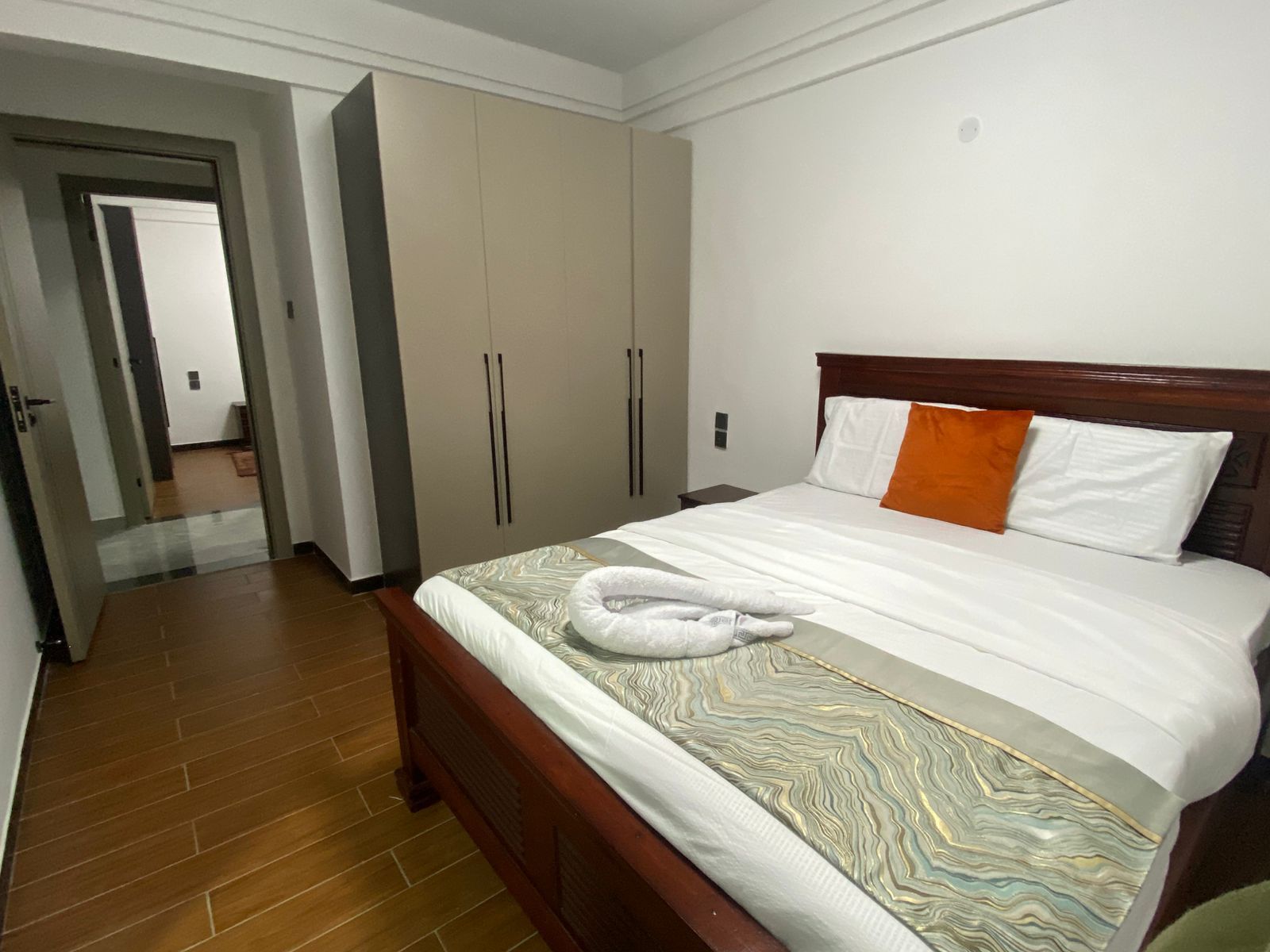 Quarto de hotel com cama de madeira, guarda-roupa amplo e banheiro visível através de uma porta aberta.