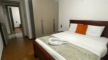 Quarto de hotel com cama de madeira, guarda-roupa amplo e banheiro visível através de uma porta aberta.