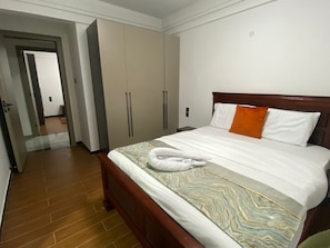 Quarto de hotel com cama de madeira, guarda-roupa amplo e banheiro visível através de uma porta aberta.