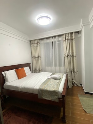 Quarto de hotel com cama, cortinas e uma luminária no teto.