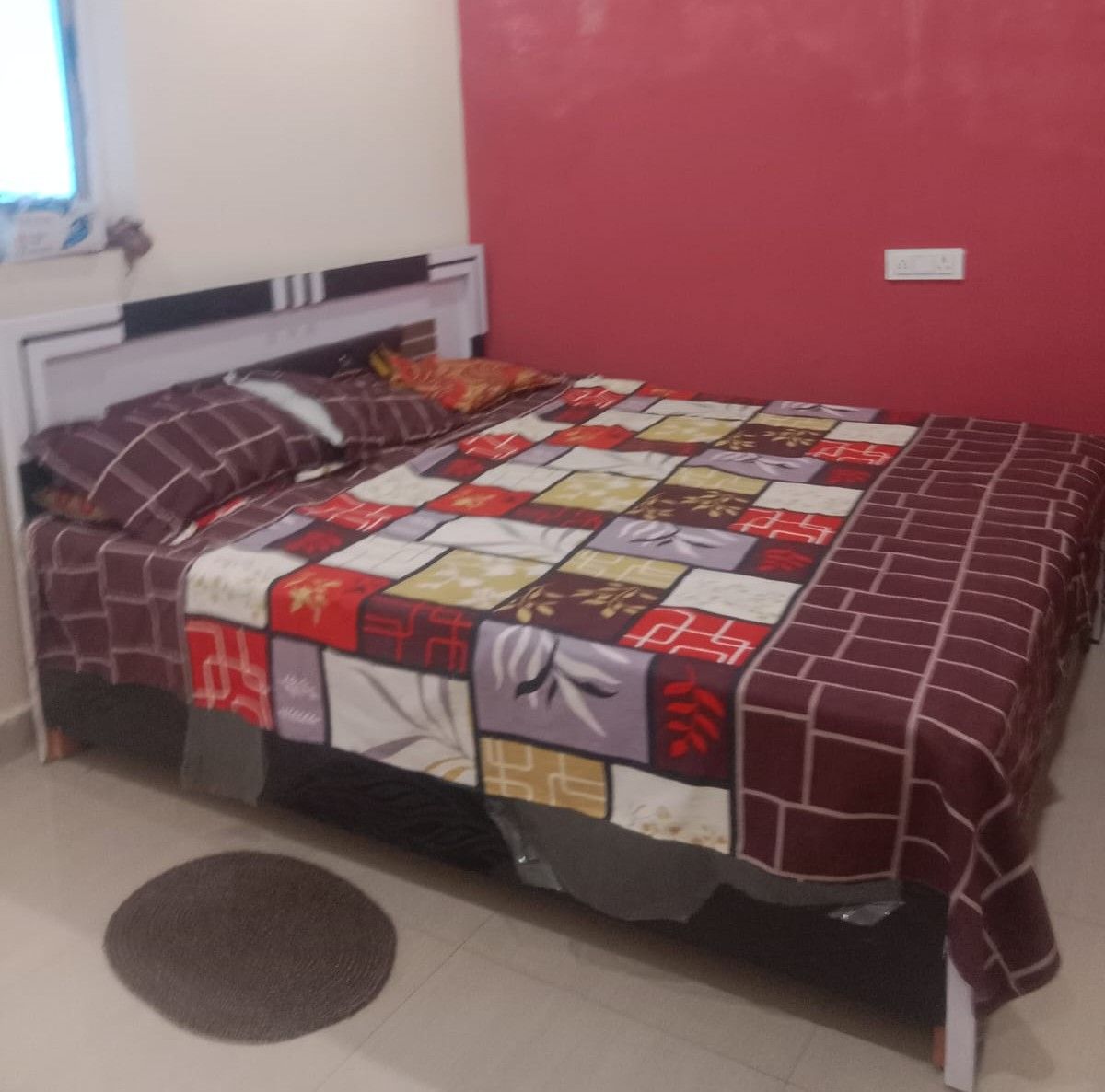 A bed with a quilt, a bedside table, and a window with blinds.