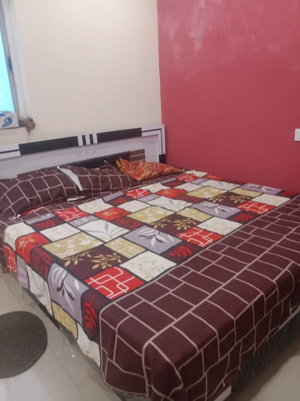 A bed with a patterned bedspread, a headboard, and a window with curtains. - Rajeshwari Hotel and Family Restaurant (Mandu)