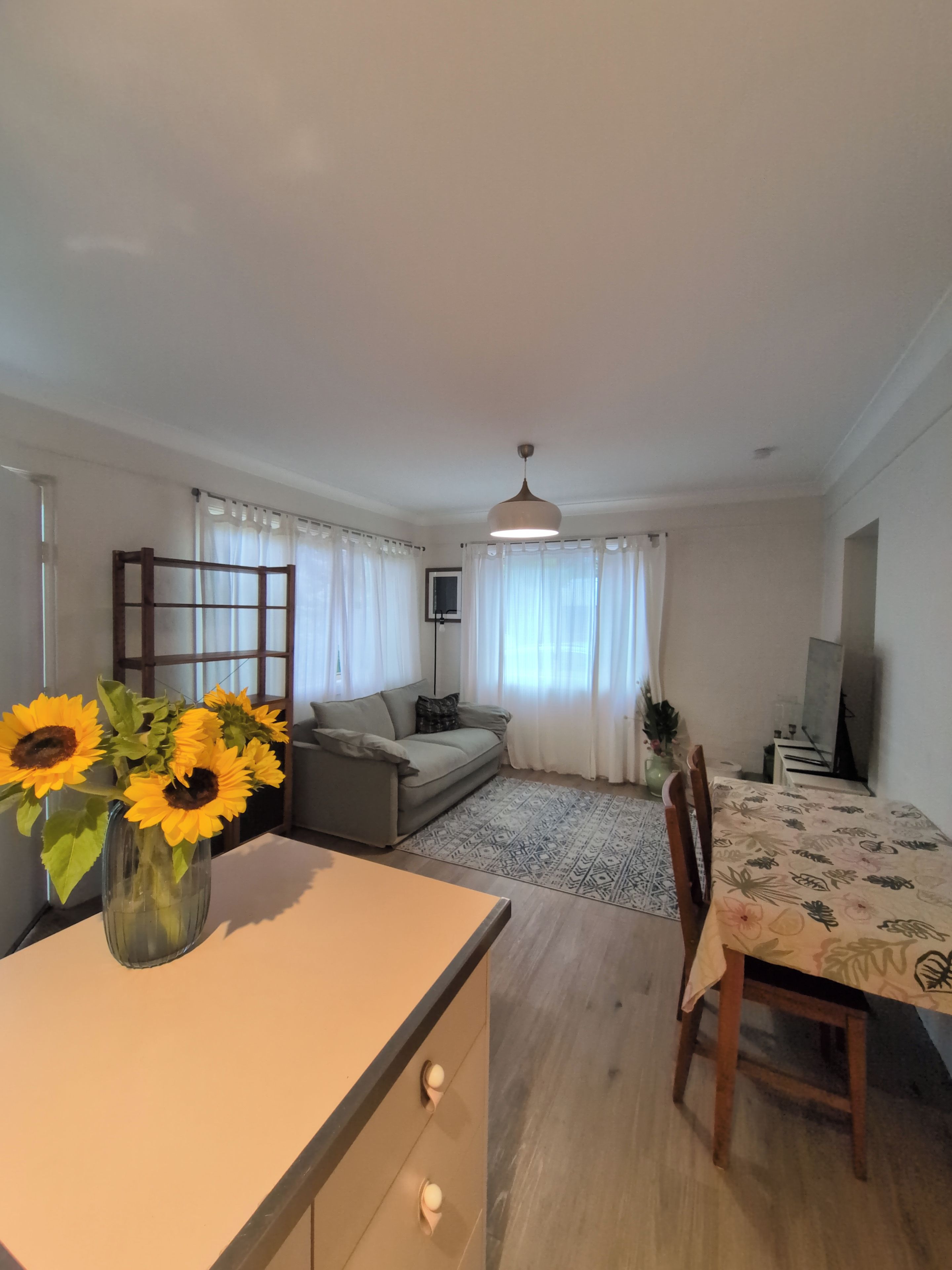 Una sala de estar con un sofá, una mesa de comedor y un jarrón con girasoles.
