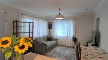 Una sala de estar con un sofá, una mesa de comedor y un jarrón con girasoles.