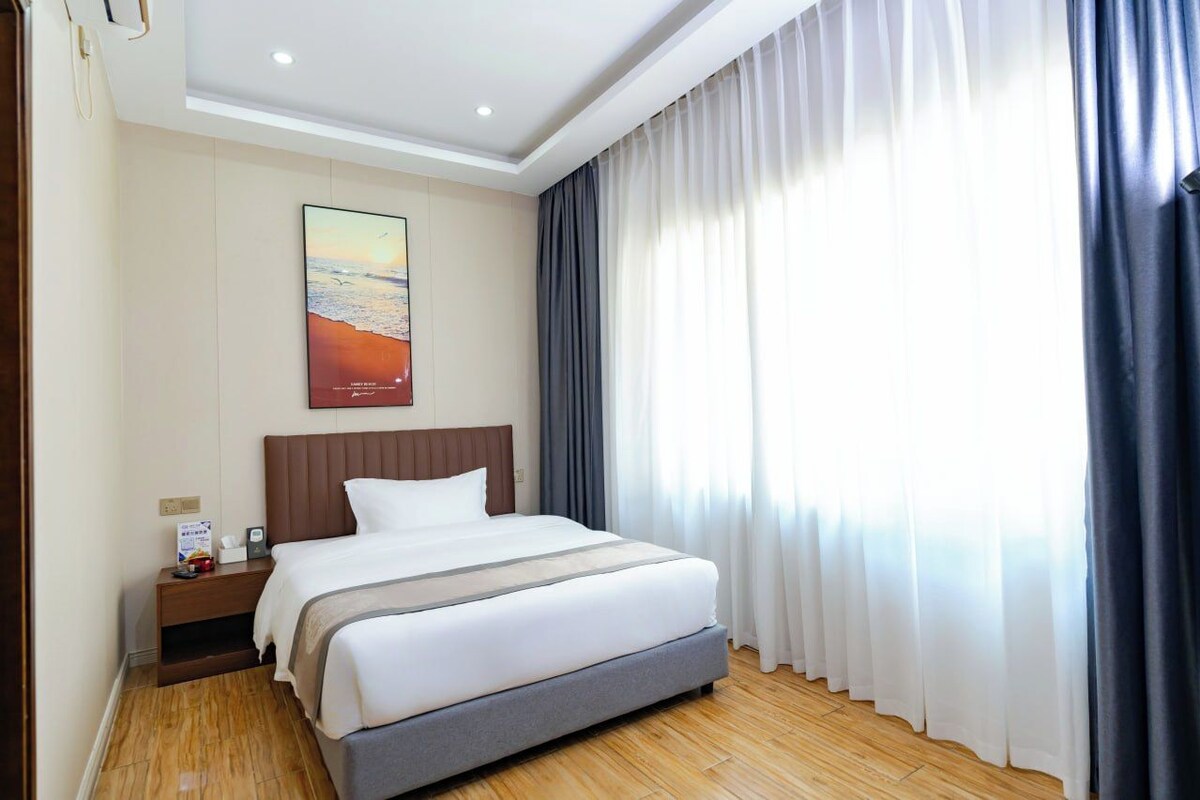 A hotel room with a bed, a nightstand, a wall-mounted TV, and a window with curtains.