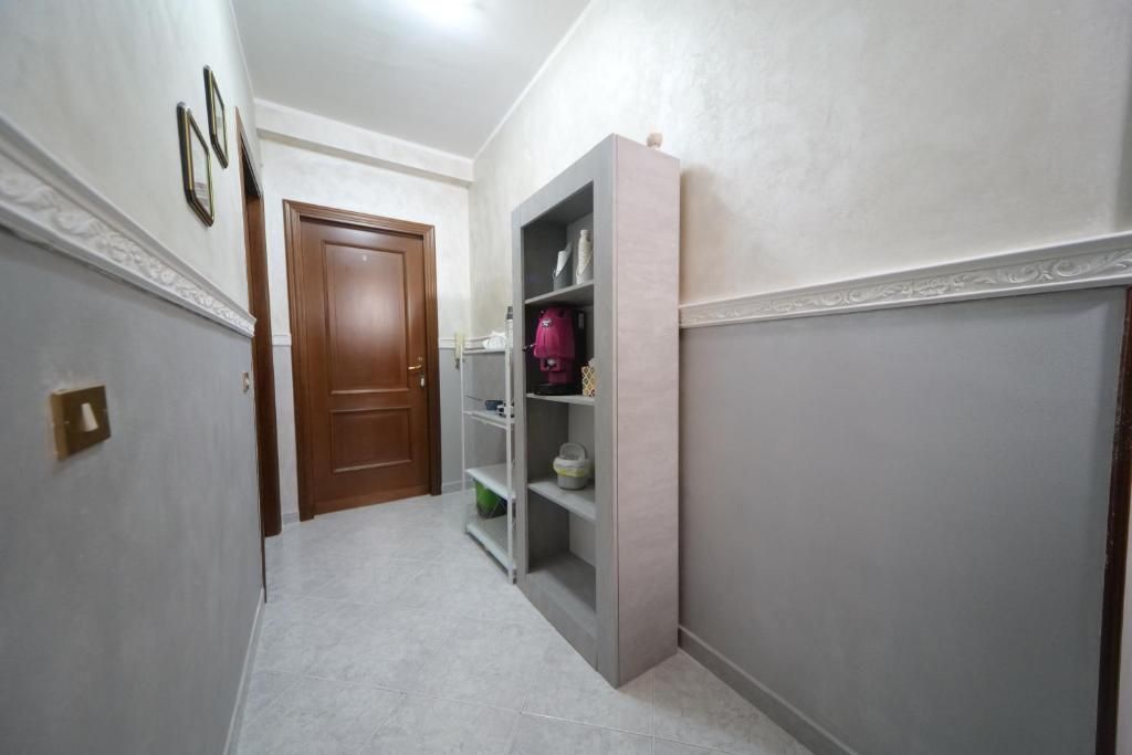 Un pasillo con una puerta de madera, un estante blanco y una pared de color claro.