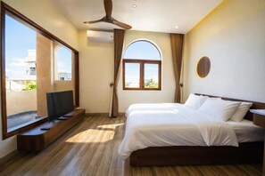 Une chambre d’hôtel avec un lit, une télévision, un ventilateur de plafond et une grande fenêtre.