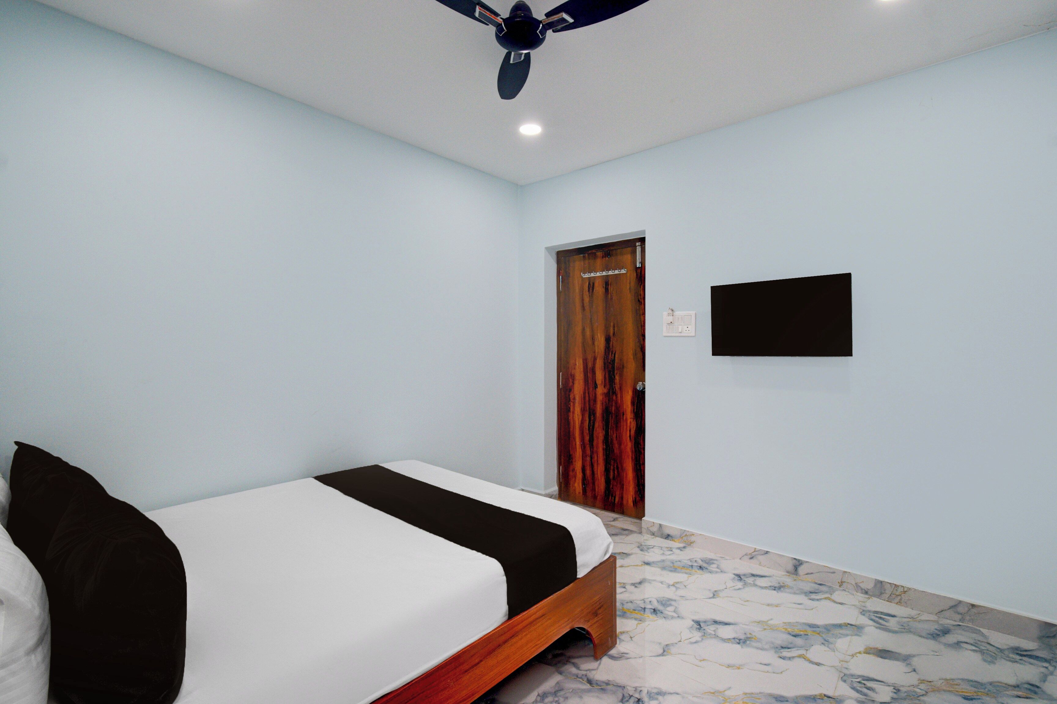A bedroom with a bed, a ceiling fan, a door, and a wall-mounted TV.
