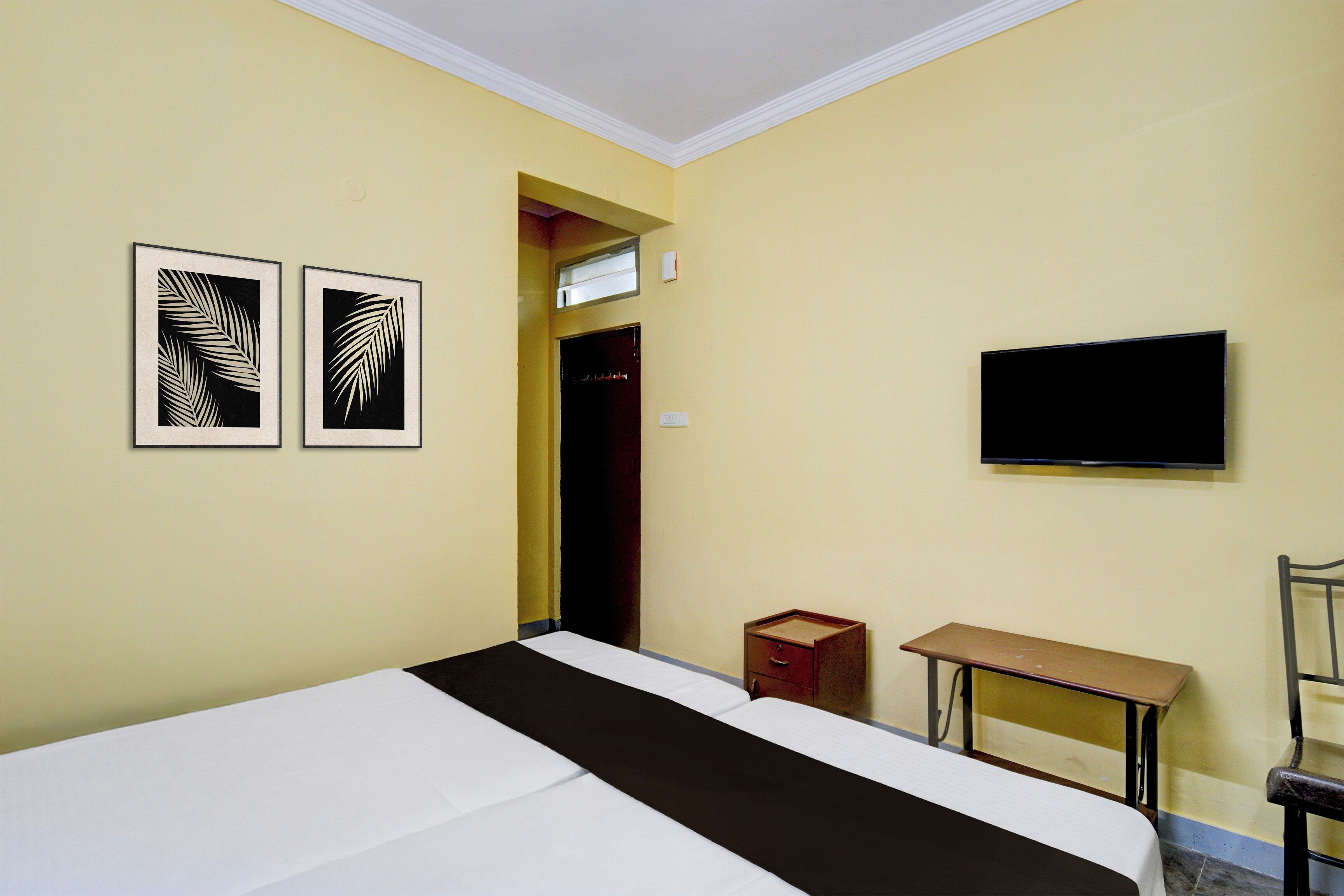A bedroom with a bed, a TV mounted on the wall, and two framed leaf patterns on the wall.