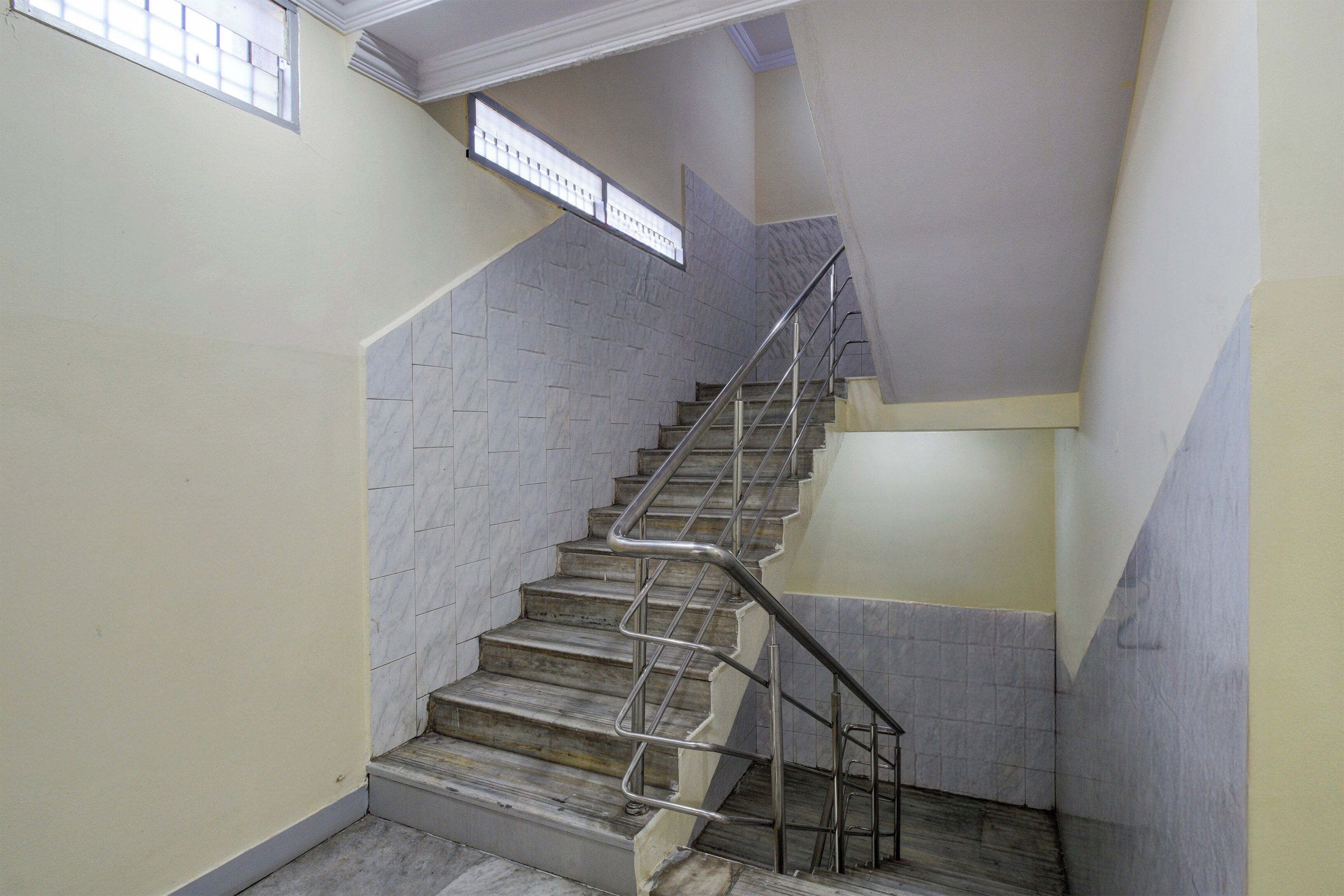 A staircase with metal handrails, marble steps, and a plain wall with a window.