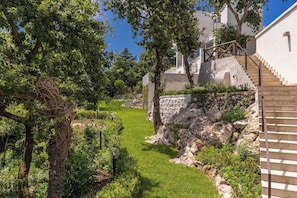 A landscaped garden with a stone wall, a grassy area, and a staircase leading to a building.