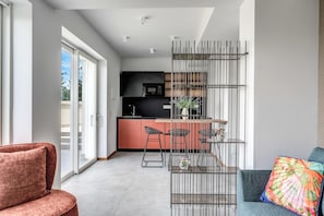 A modern apartment with a kitchen, a dining area with a metal partition, and a living room with a sofa and a colorful cushion.
